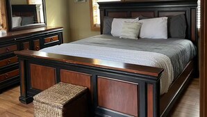 Een slaapkamer met een groot bed, houten meubels, een plafondventilator en een raam met jaloezieën.
