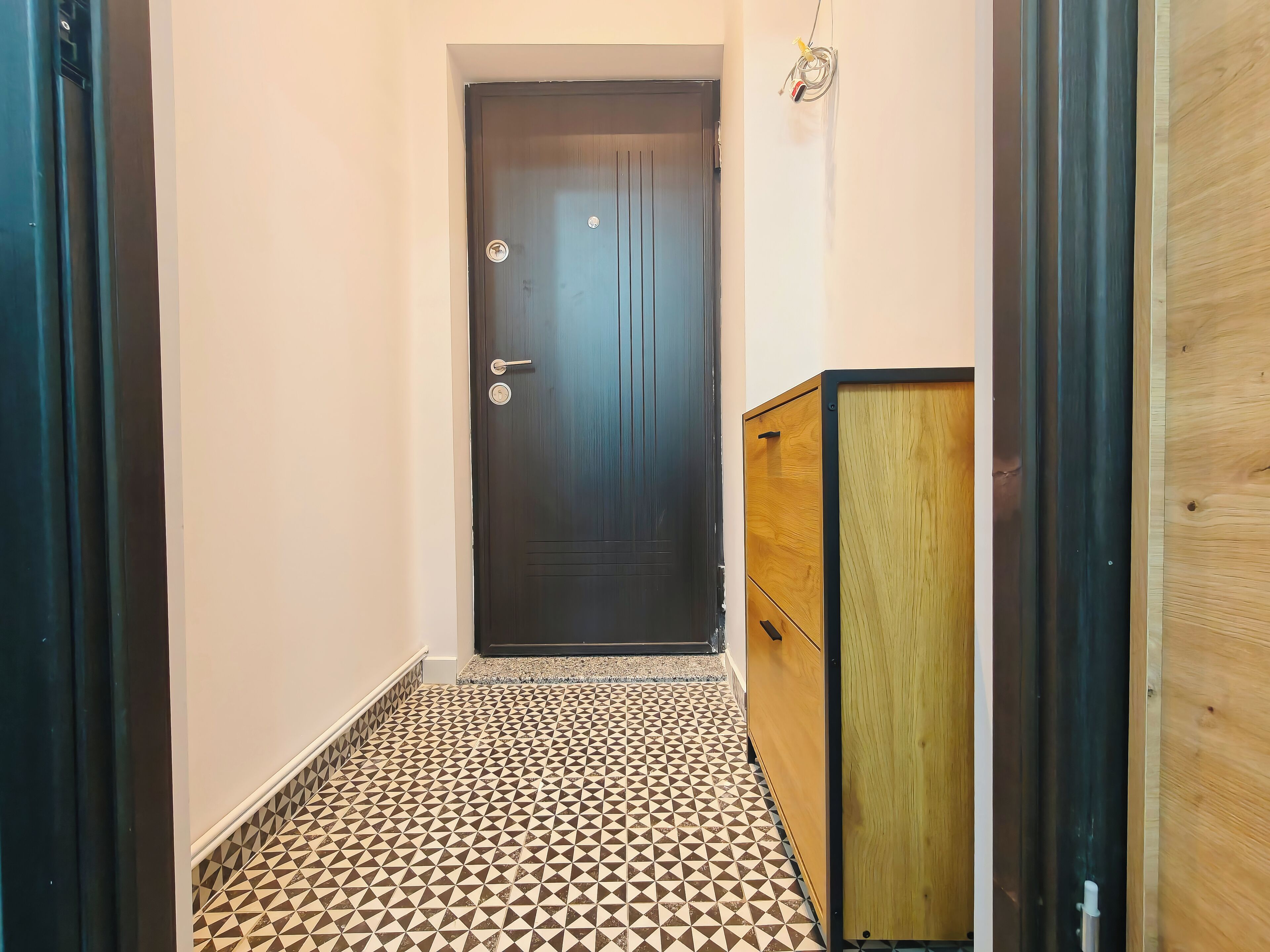 Ein Korridor mit einem gemusterten Boden, einer dunklen Holztür und einem Holzschrank.