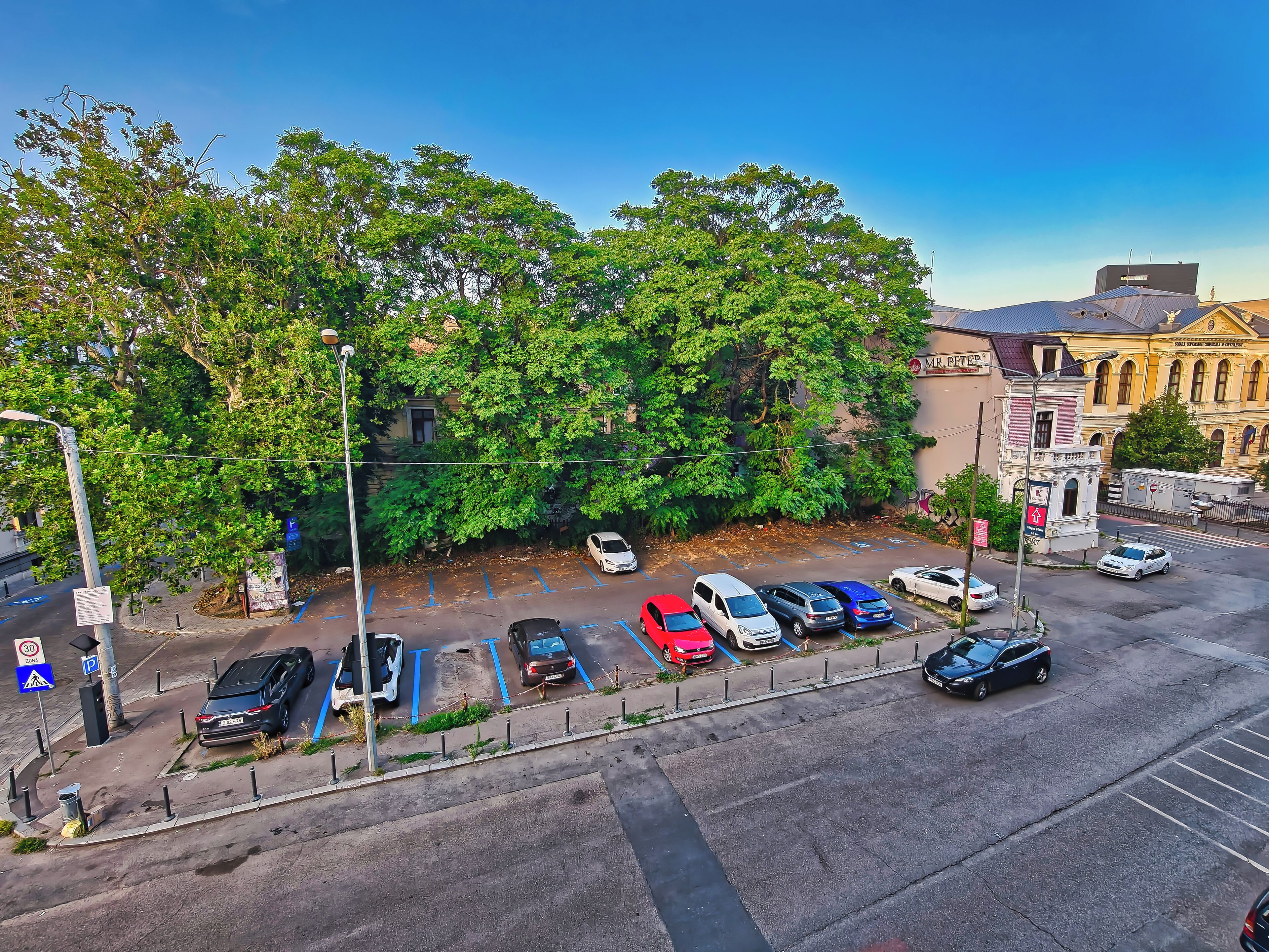 Ein Parkplatz mit verschiedenen Autos, einer Fußgängerüberweg und ein Gebäude mit klassischer Architektur im Hintergrund.