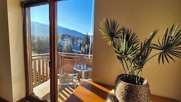 A balcony with a wooden table and chairs, a potted plant, and a view of a mountain and buildings.