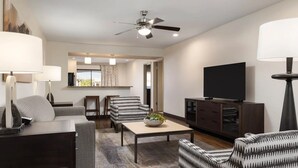 Ein modernes Wohnzimmer mit Sofa, Sesseln, Couchtisch, Fernseher und Deckenventilator.