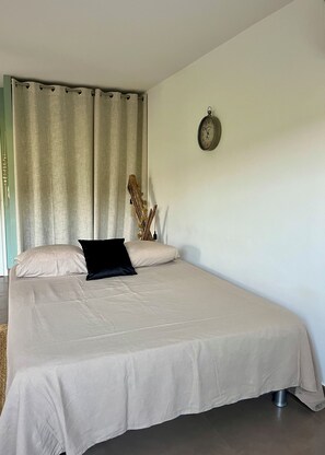 A bedroom with a bed, curtains, a wall clock, and a decorative wooden piece. - 5 minutes from the beach, beautiful studio in a quiet, secure residence (Grosseto-Prugna)