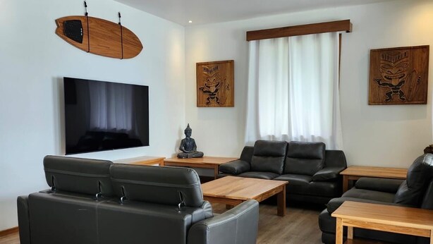 Una sala de estar moderna con un televisor de pantalla plana, sofás de cuero, mesas de centro de madera y decoración mural.