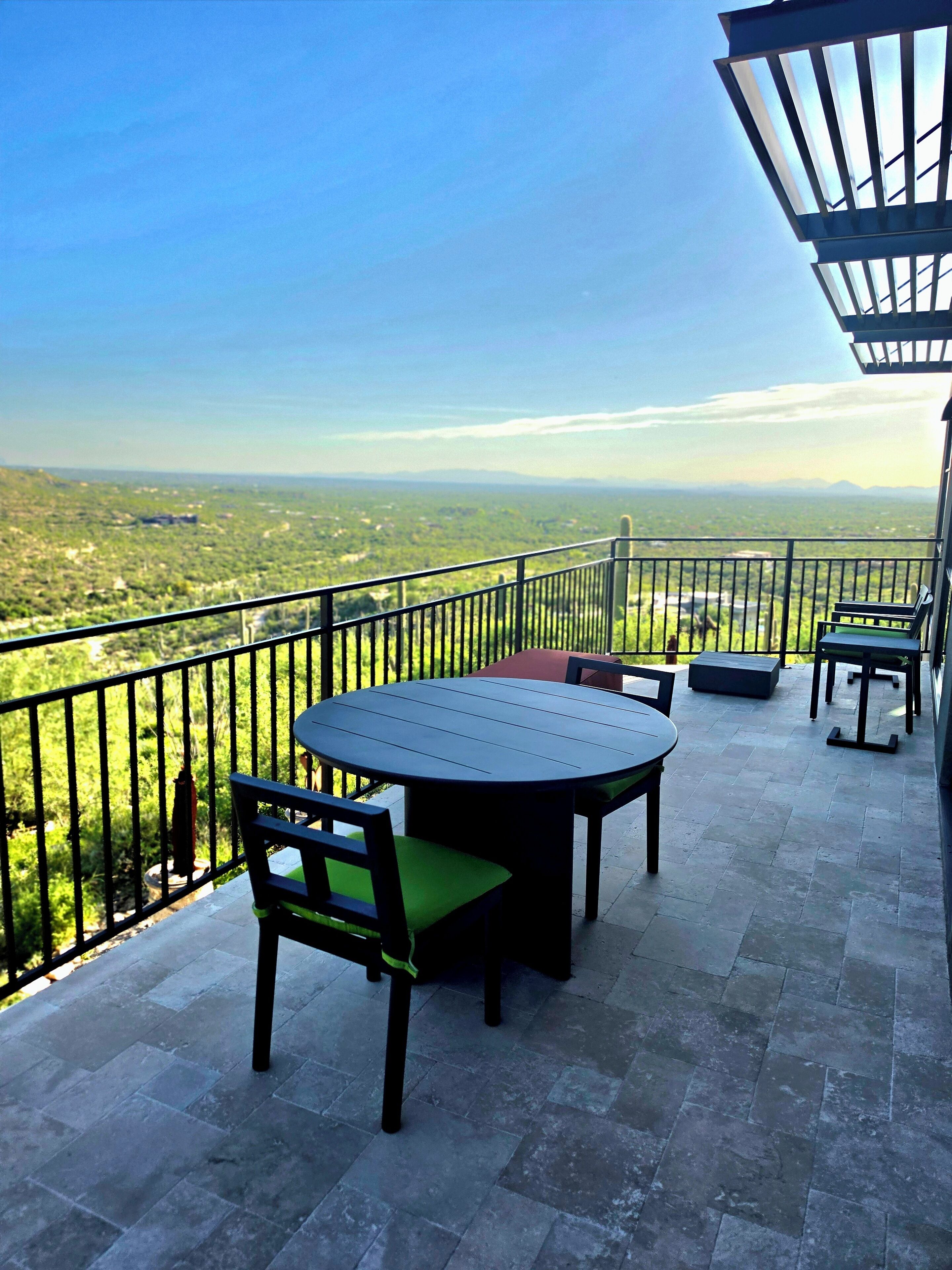 Ein Balkon mit Tisch und Stühlen, Blick auf eine grüne Landschaft und einen klaren Himmel.