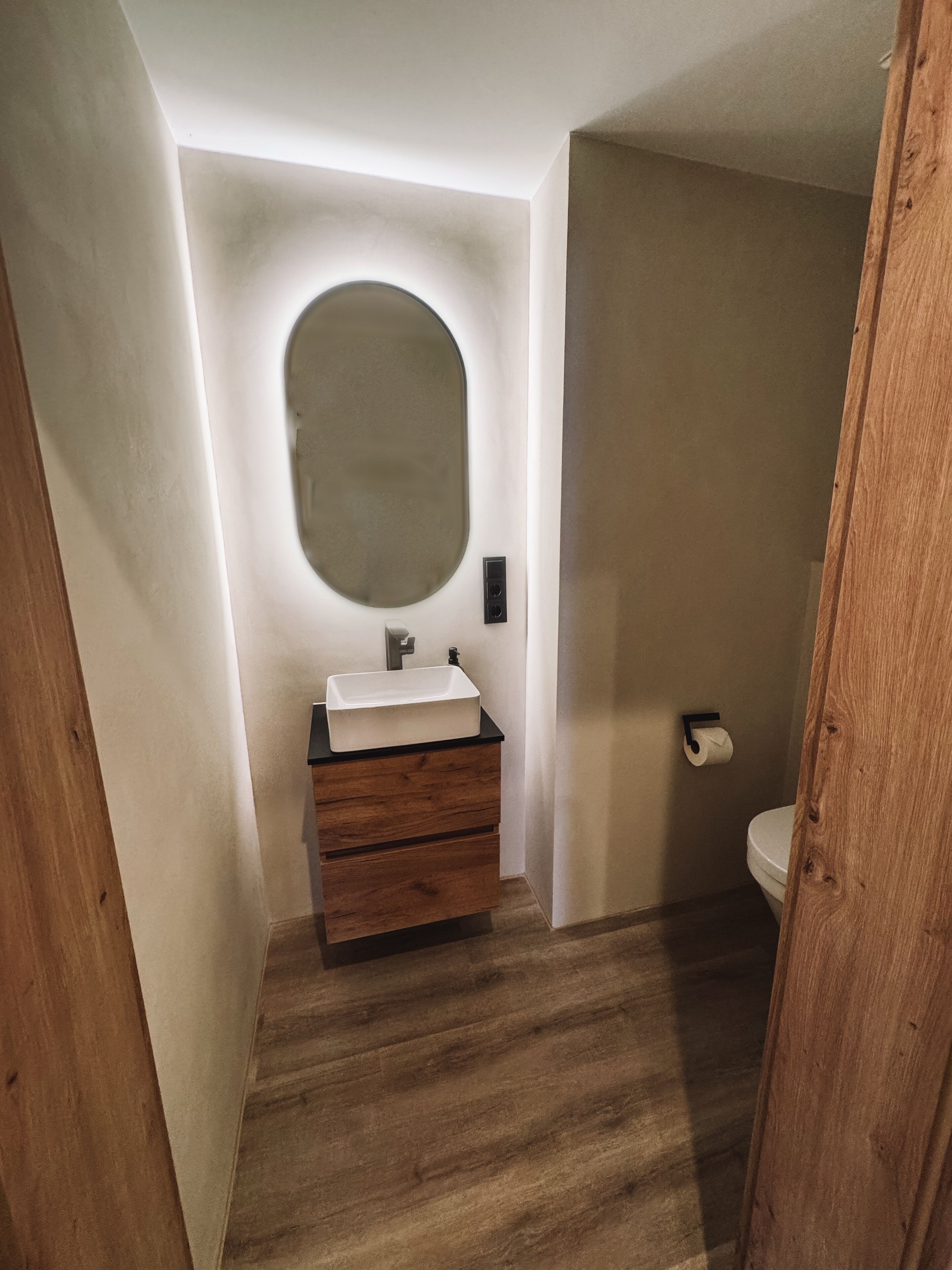 Une salle de bain avec un meuble-lavabo en bois, un miroir rond et des toilettes.