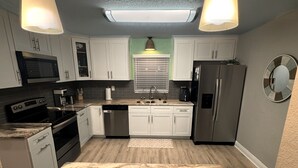 A modern kitchen with white cabinets, a stainless steel refrigerator, a microwave, and a dishwasher. - Dunedin Palm Retreat •1 Mile to Downtown Dunedin •Walk to Pinellas Trail & Beach (Clearwater)
