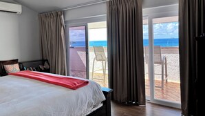 Une chambre avec un lit, un ventilateur de plafond et une vue sur la plage, accessible par une porte-fenêtre coulissante.
