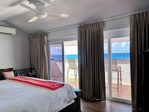 Ein Schlafzimmer mit Bett, Deckenventilator und Blick auf den Strand durch eine Schiebetür.