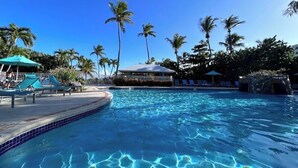 Une piscine d’un bleu éclatant, entourée de palmiers et de chaises longues.