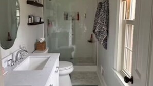 Une salle de bain avec un lavabo blanc, un miroir et des toilettes. Il y a également un espace douche avec une porte en verre.