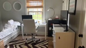 Une chambre à coucher comprenant un lit, un bureau, une chaise, un téléviseur et une fenêtre avec des stores.