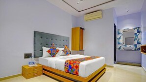 A modern bedroom with a tufted headboard, a wooden bedside table, a large bed with colorful geometric bedding, and a bathroom with a marble backsplash and a sink. - Hotel Nidhivan Palace  (Surat)