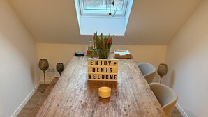 Una mesa de comedor de madera con un cartel que dice 'Enjoy Denis Welcome', un jarrón con tulipanes rojos y un tragaluz arriba.