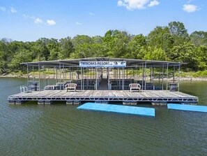 Una plataforma flotante con un área de estar techada, un letrero que dice "THINOAKS RESORT" y un muelle que se extiende hacia el agua.