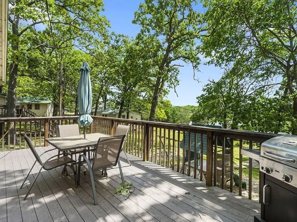 A wooden deck with outdoor furniture, a grill, and a view of trees and hills.