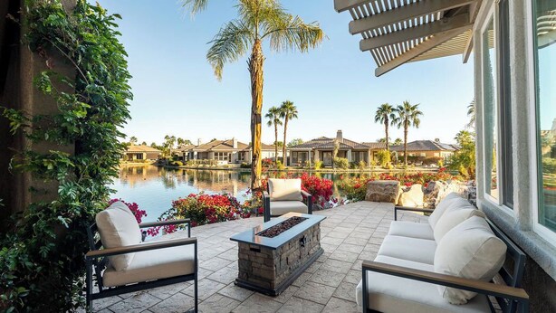 A patio with outdoor seating, a fire pit, and a view of a pool and buildings in the background.