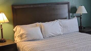 A neatly made bed with a dark headboard, two bedside lamps, and a green wall.