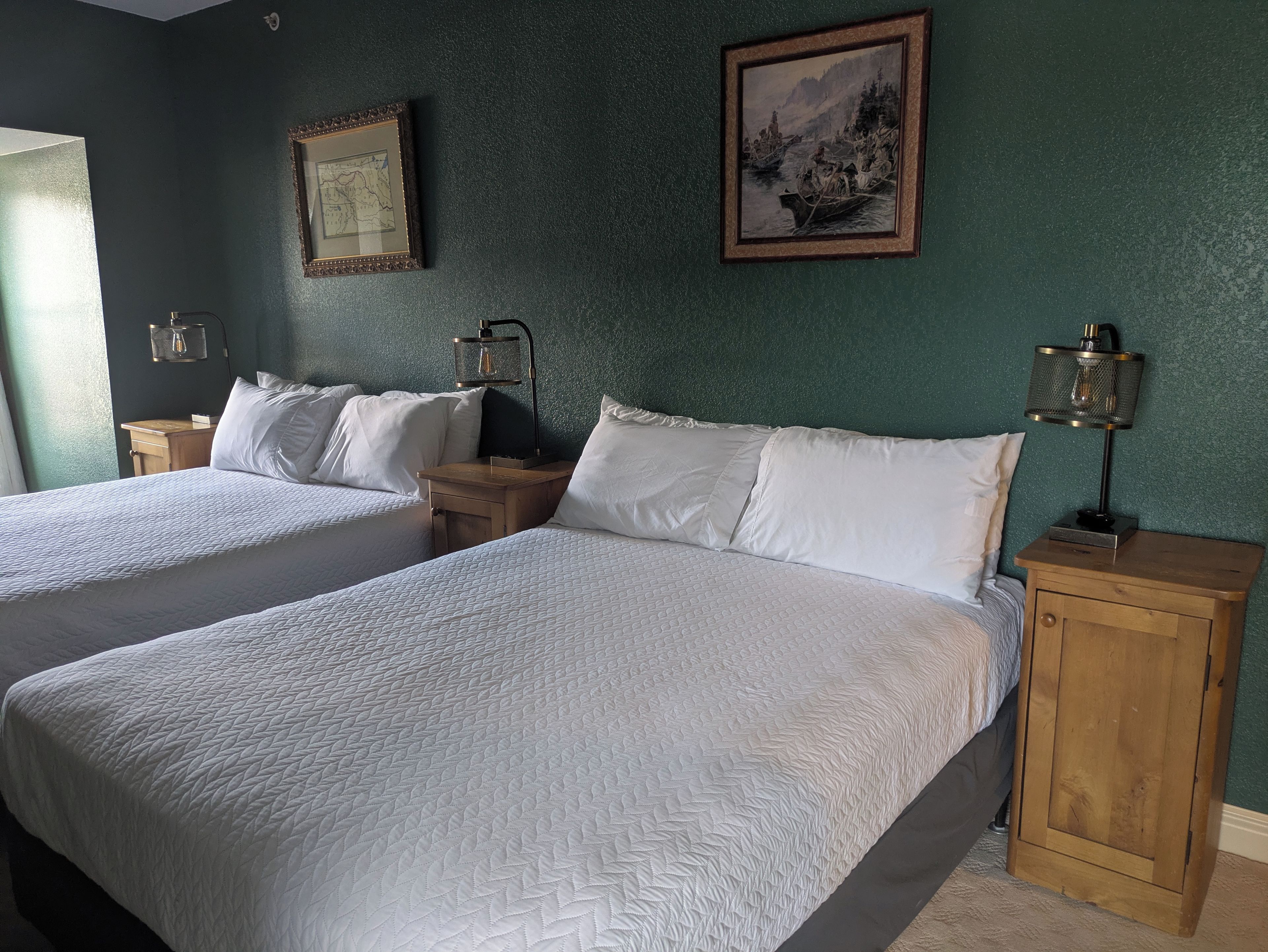 A hotel room with two beds, a map, a lamp, and a painting on the wall.