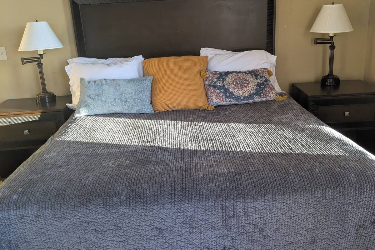 Un letto ben rifatto con copriletto decorato, una testiera scura e due comodini con lampade.