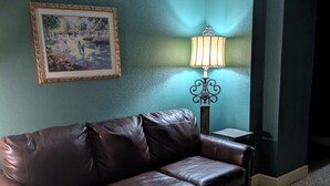 Ein Zimmer mit einem braunen Ledersofa, einem gerahmten Bild an der Wand, einer Stehlampe und einem gemusterten Teppich.