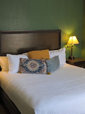 A neatly made bed with a white quilt, a variety of pillows, and a bedside lamp. - Saint George Hotel (Weston)
