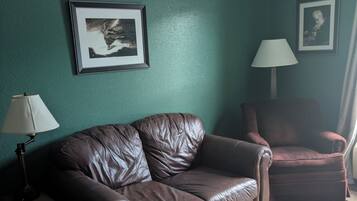 A living room with a brown leather sofa, a matching armchair, a small wooden coffee table, and two wall-mounted lamps.