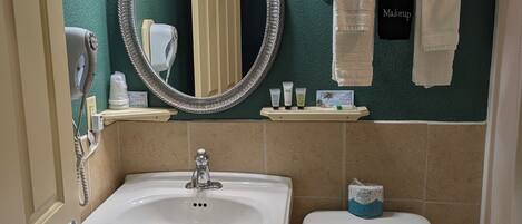 A bathroom with a sink, toilet, and a mirror with lights. There are towels and toiletries on the wall.