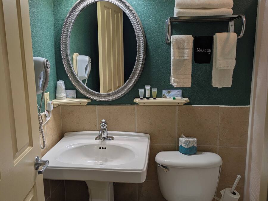 A bathroom with a sink, toilet, and a mirror with lights. There are towels and toiletries on the wall.