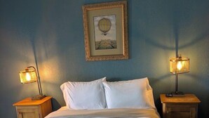 A bed with white linens, two bedside tables with lamps, a framed picture on the wall, and a blue wall. - Saint George Hotel (Weston)