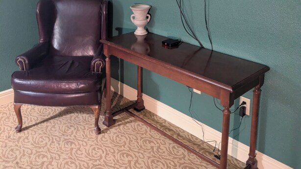 A room with teal walls, a leather armchair, a wooden table, and a mounted television. - Saint George Hotel (Weston)