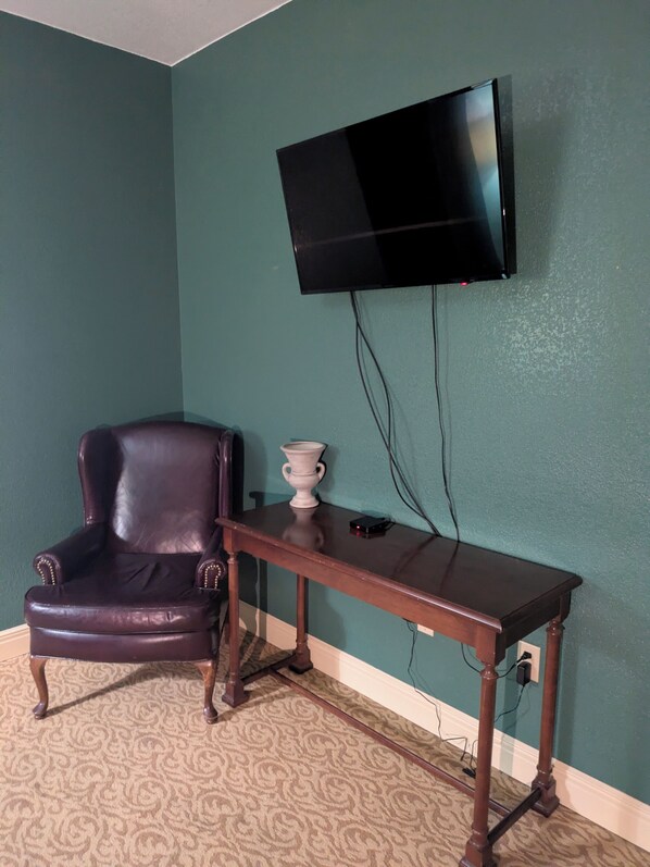 A room with teal walls, a leather armchair, a wooden table, and a mounted television. - Saint George Hotel (Weston)