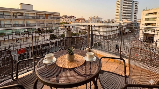Un balcon avec une table et des chaises, une plante en pot et deux tasses.