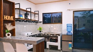 Una cocina moderna con horno empotrado, dispensador de agua y refrigerador. Cuenta con una barra con dos sillas y una pequeña mesa.