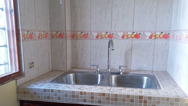 A kitchen with two stainless steel sinks, a tiled backsplash with fruit designs, and wooden cabinets. - Serene studio in Volcán perfect for a relaxing getaway. Enjoy a warm bath. (Volcán)