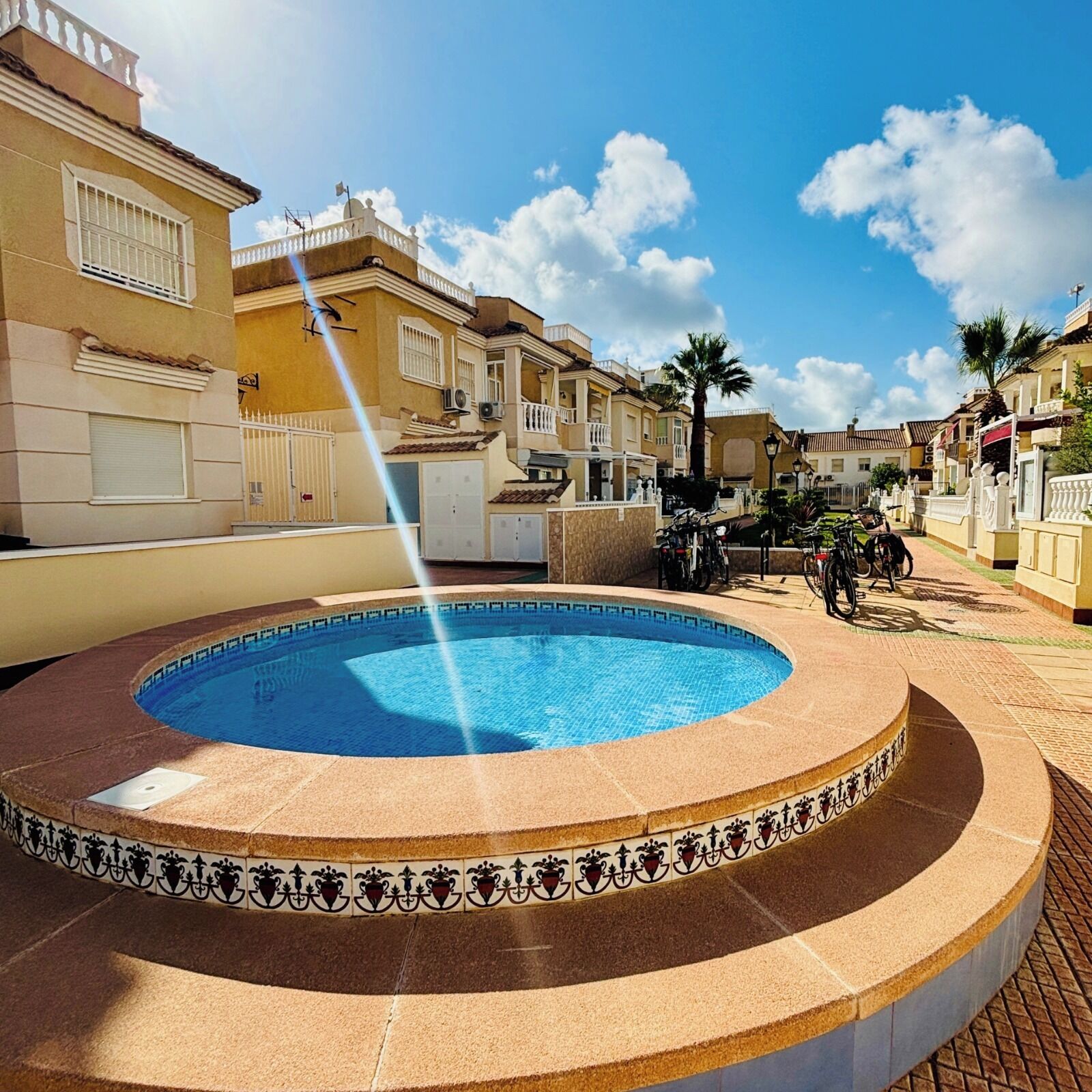 Une piscine avec une fontaine, entourée d’immeubles dotés de balcons, sous un ciel dégagé.