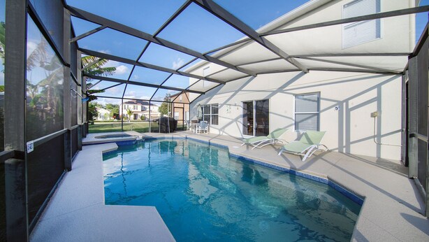 Une piscine entourée de parois en verre, un patio couvert et une vue sur un quartier résidentiel.
