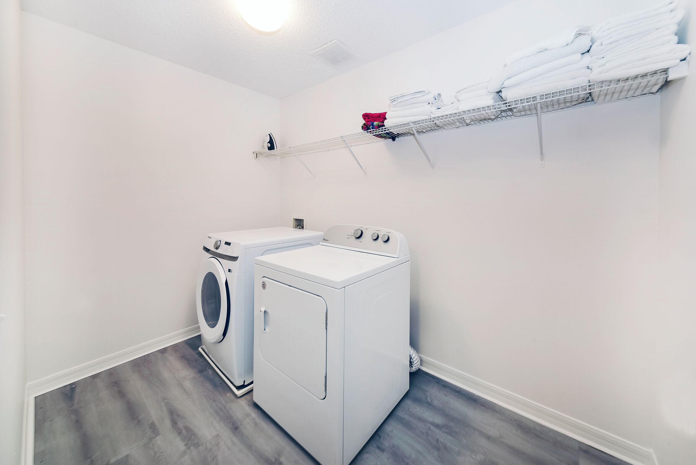 A laundry room with a front-loading washer and dryer, a shelf with folded towels, and a small ironing board.