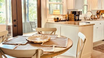 Una cocina moderna con armarios blancos, una mesa de comedor de madera con individuales y vistas al exterior a través de amplios ventanales.
