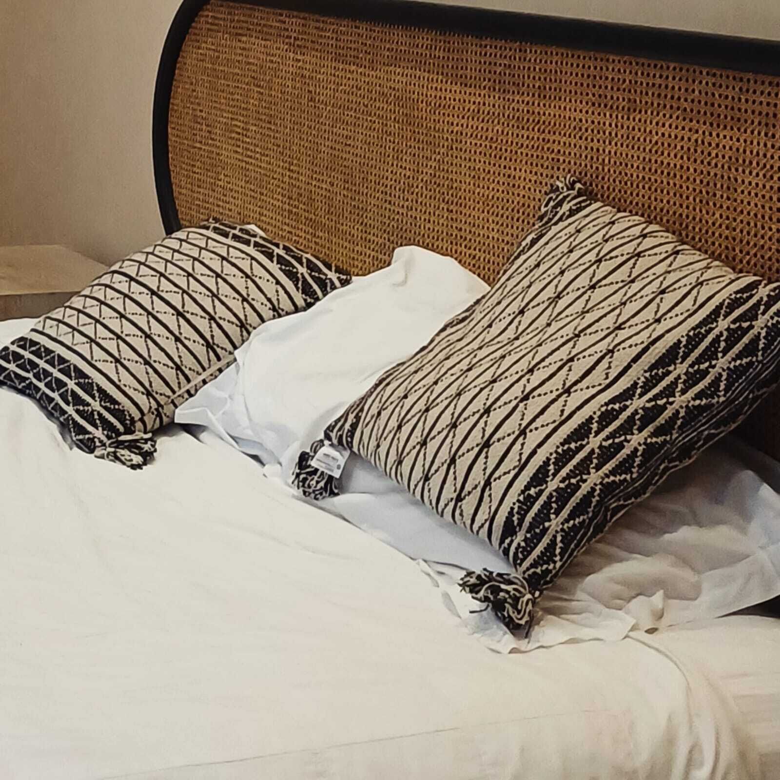 A bed with white bedding and two patterned pillows.