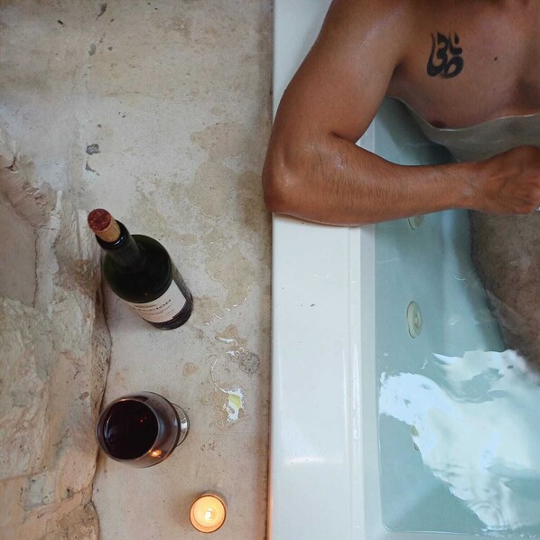 A bathtub with a person, a bottle of wine, a glass of wine, and a lit candle. - Casa Josefina (Hunucmá)