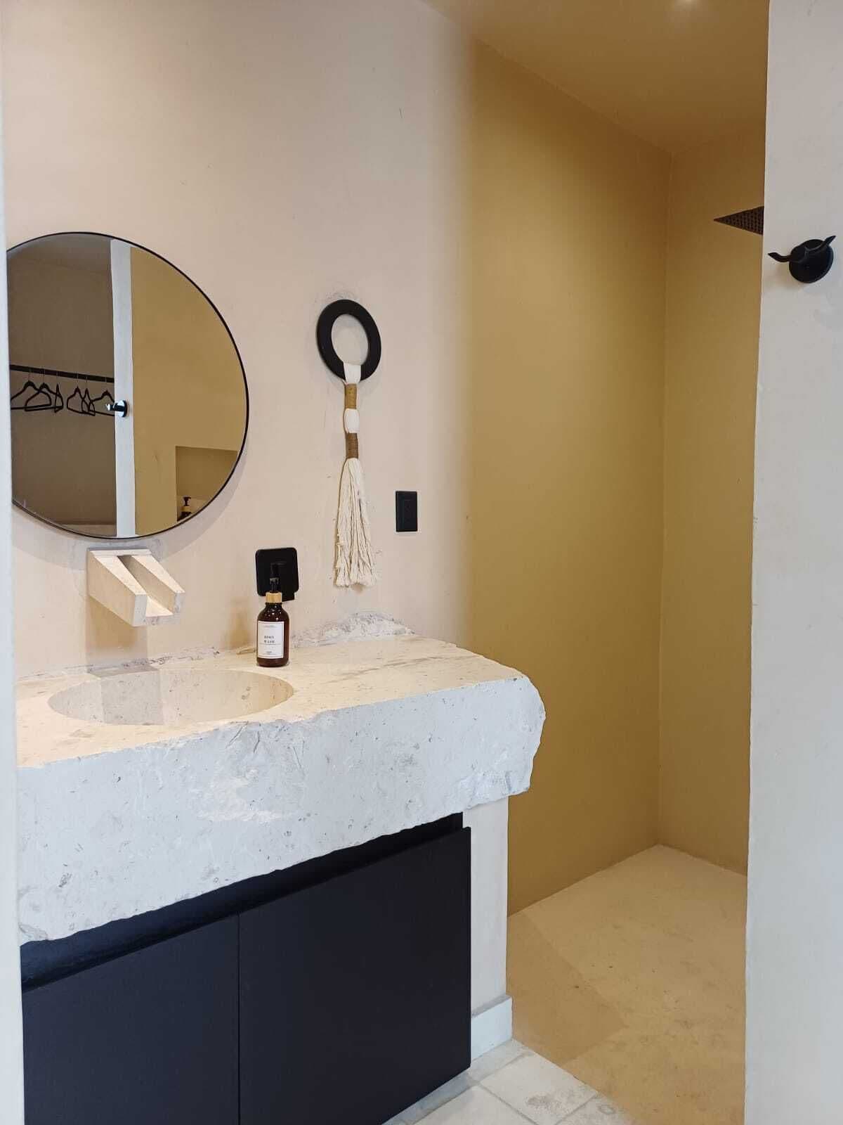 A bathroom with a round mirror, a towel ring, a bottle of soap, and a black cabinet.