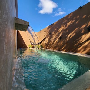 A swimming pool with clear water, surrounded by walls and a hammock.