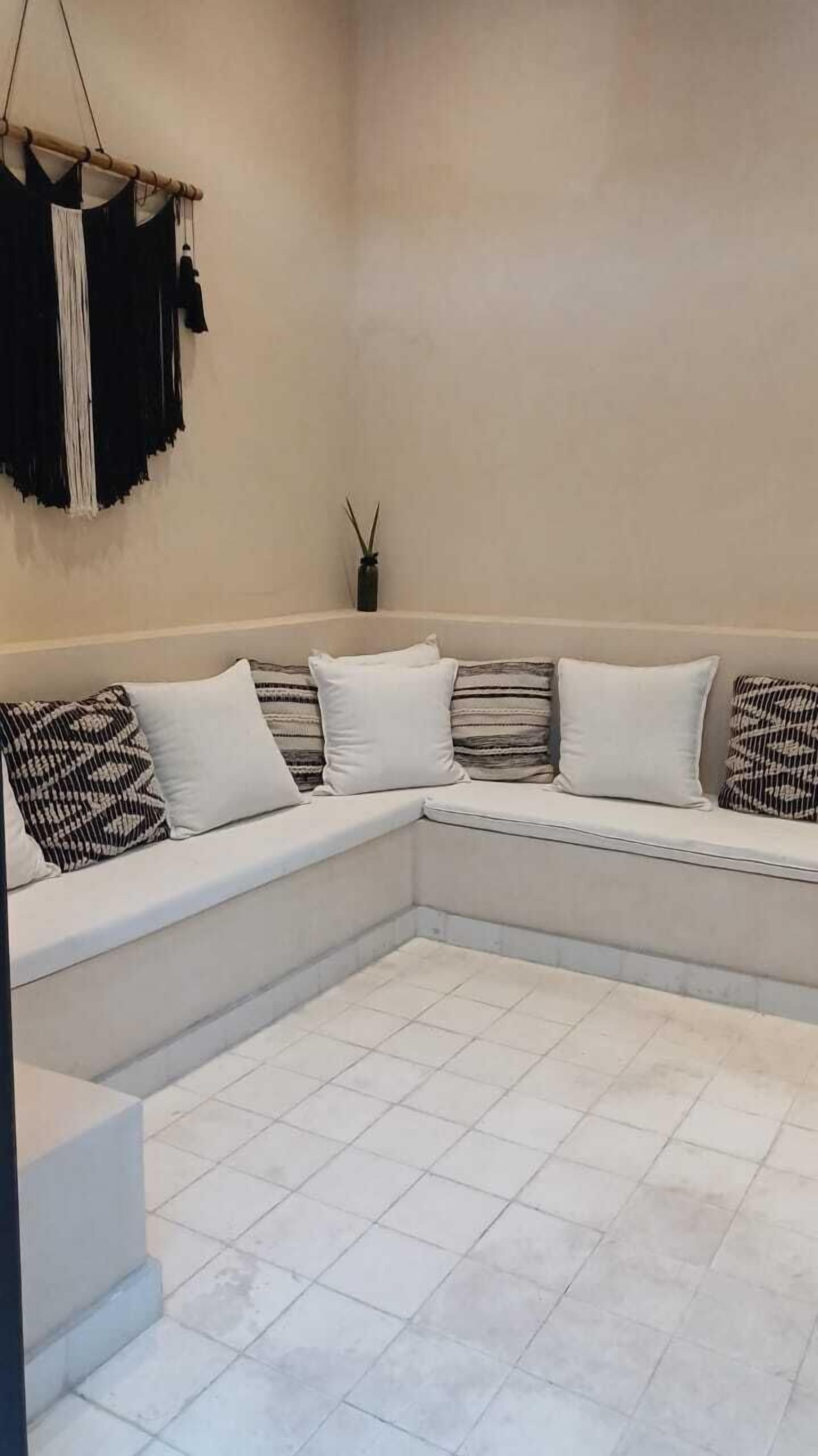 Un'area salotto angolare con divano bianco, cuscini decorati e pavimento piastrellato.