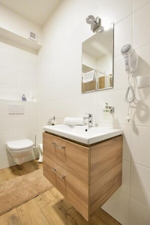 A modern bathroom with a wooden vanity, a white sink, a mirror, and a hairdryer mounted on the wall. - Penzion U Smrku Luleč (Luleč)