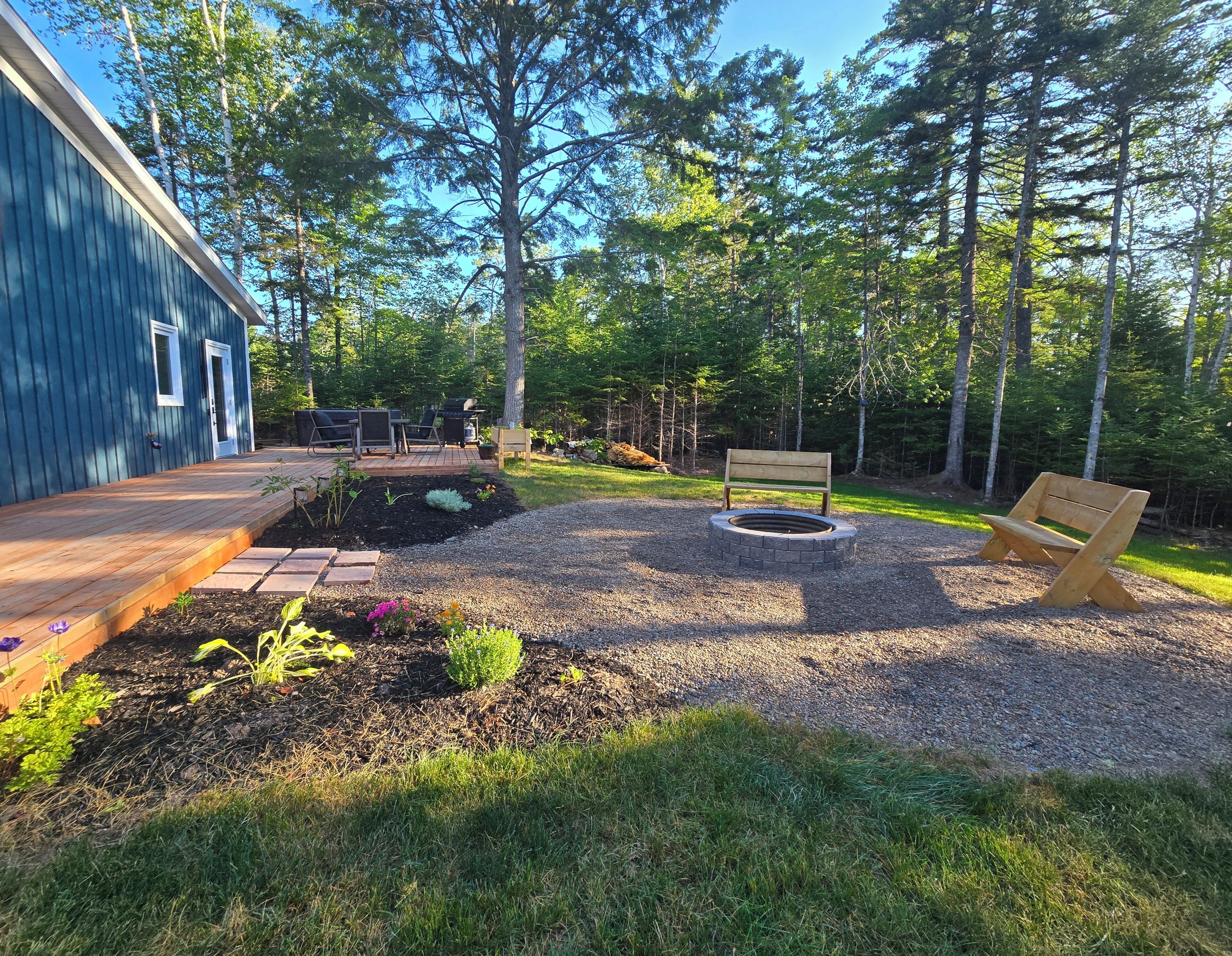 A backyard with a deck, outdoor seating, a fire pit, and a bench.