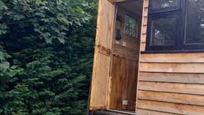 Una cabaña de madera con la puerta abierta, rodeada de follaje denso.