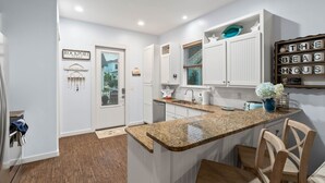 A modern kitchen with white cabinetry, granite countertops, and a built-in island with bar stools. - Waterfront Community with Private Pier + Pool (Rockport)