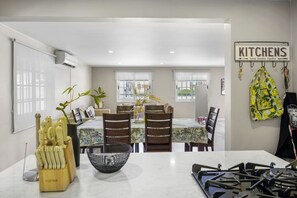 A modern kitchen with a dining area, featuring a kitchen sign, a stove, and a dining table with chairs. - Amazing 3-Bedroom Beach House 7-min Drive to the Ocean & Palm Trees Up to 8 Ppl (Noord)