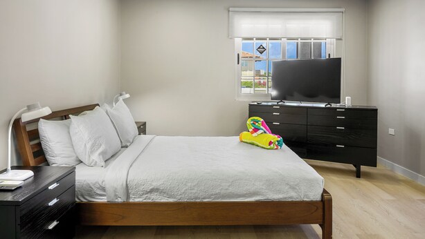 Ein Schlafzimmer mit Bett, Kommode, Fernseher und einem Fenster mit Jalousien.