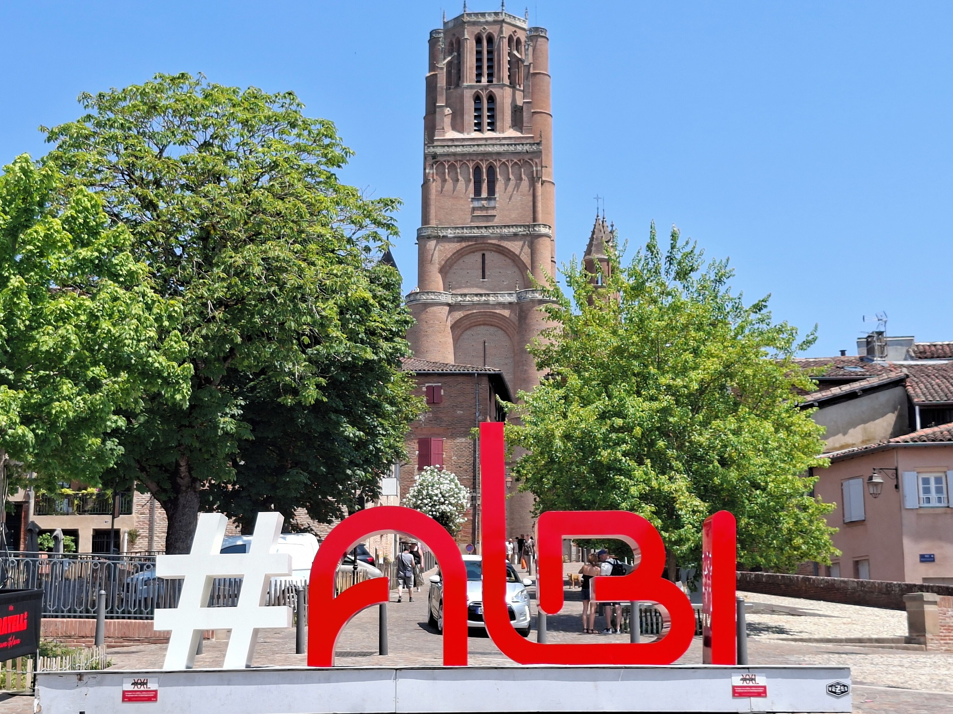Eine historische Kirche mit hohem Glockenturm, umgeben von Bäumen und einer roten Skulptur.